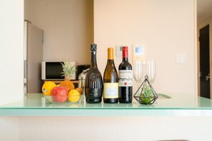 A glass table with bottles of wine, a pineapple, oranges, and a small plant.