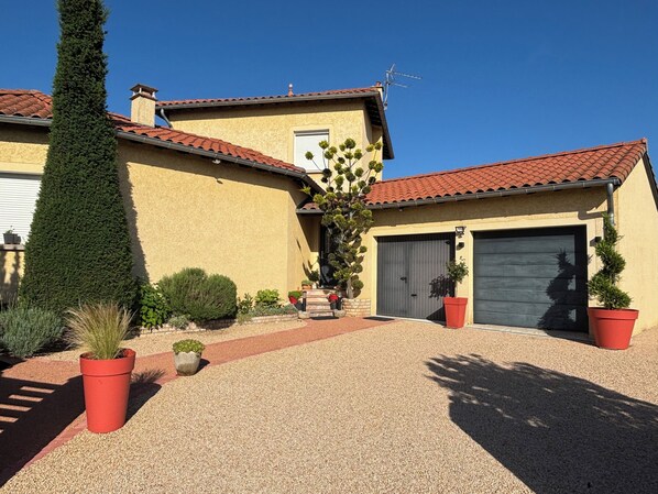 A two-story house with a red-tiled roof, a garage, and a gravel driveway.