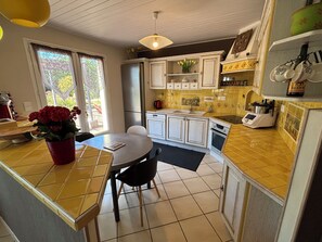A kitchen with white cabinets, a dining table, chairs, a refrigerator, an oven, and a sink.