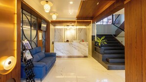Um hall moderno com um balcão de recepção, um sofá azul, uma escadaria e um candelabro.