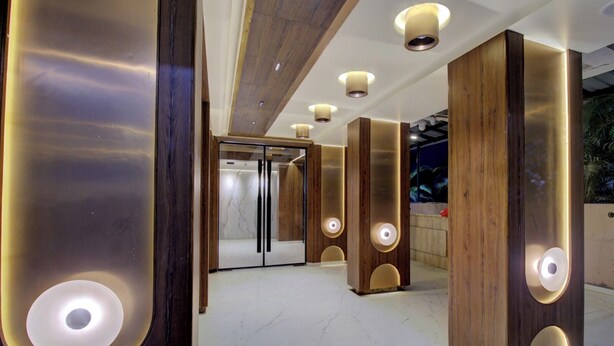 Um lobby moderno com piso de mármore, paredes de detalhes em madeira e iluminação embutida.