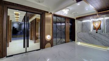 A modern hotel lobby with a marble floor, wooden accents, and a reception area with a heart-shaped light fixture.