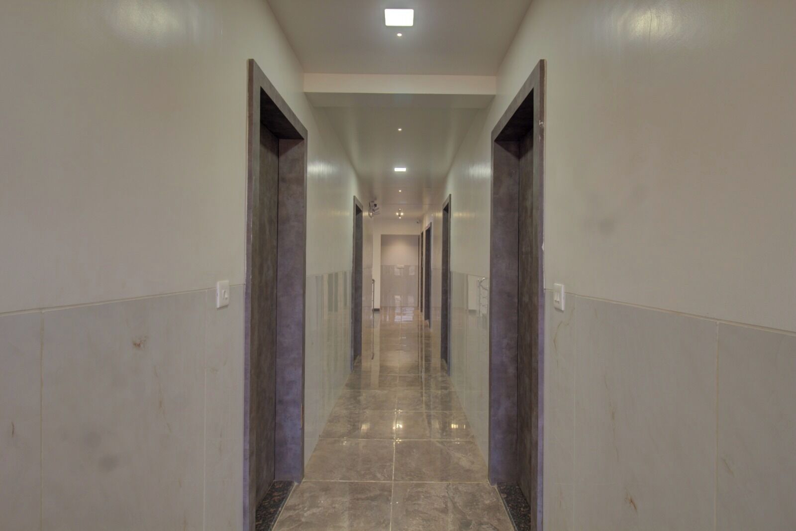 A long, narrow hallway with a polished marble floor and dark-colored doors on either side.