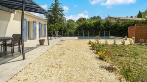 Eine überdachte Terrasse mit Sitzgelegenheiten im Freien, ein Schwimmbecken und ein Kiesbereich mit Pflanzen.