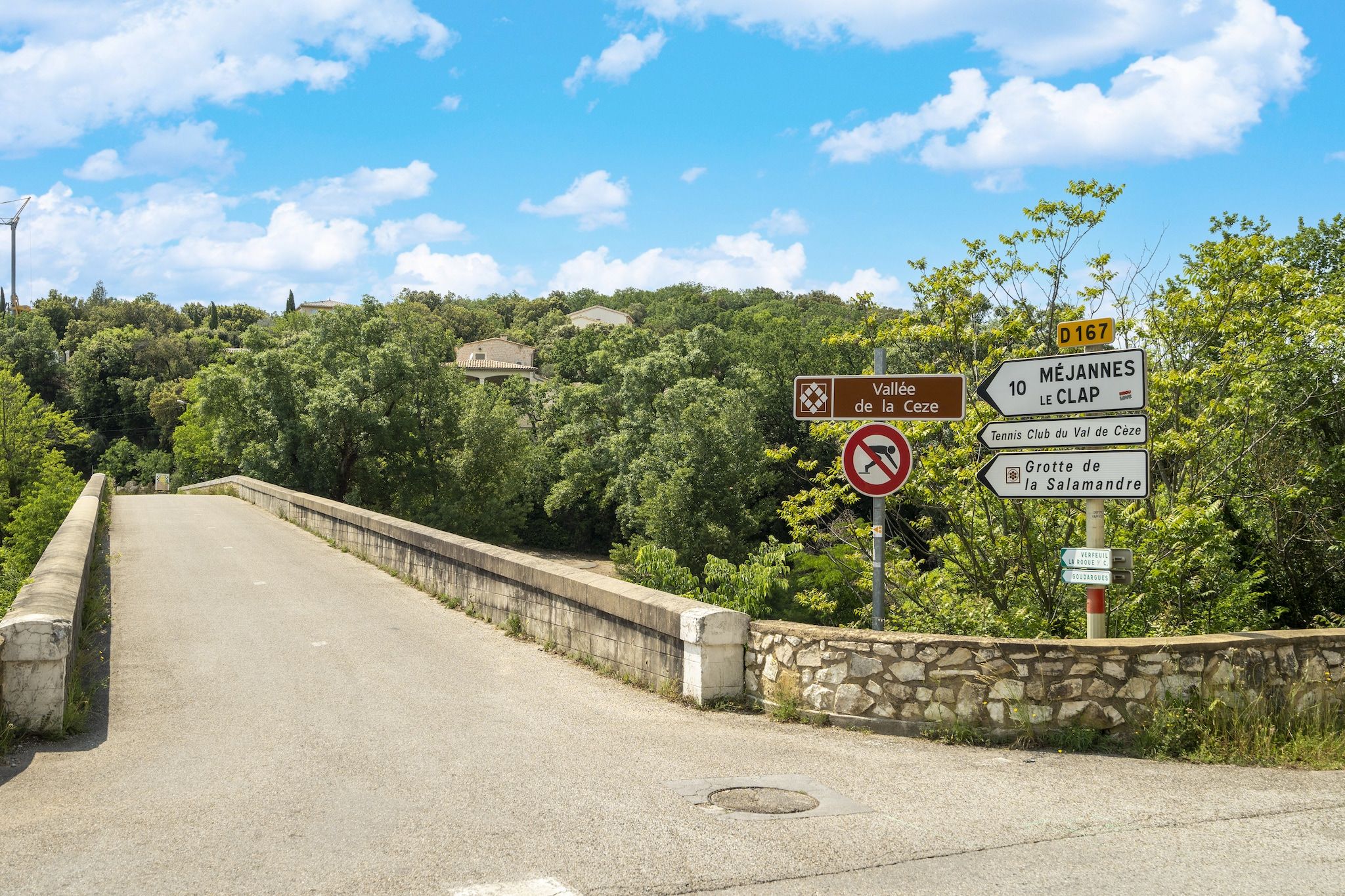A bridge with directional signs, a no-sitting sign, and a stone wall on one side.