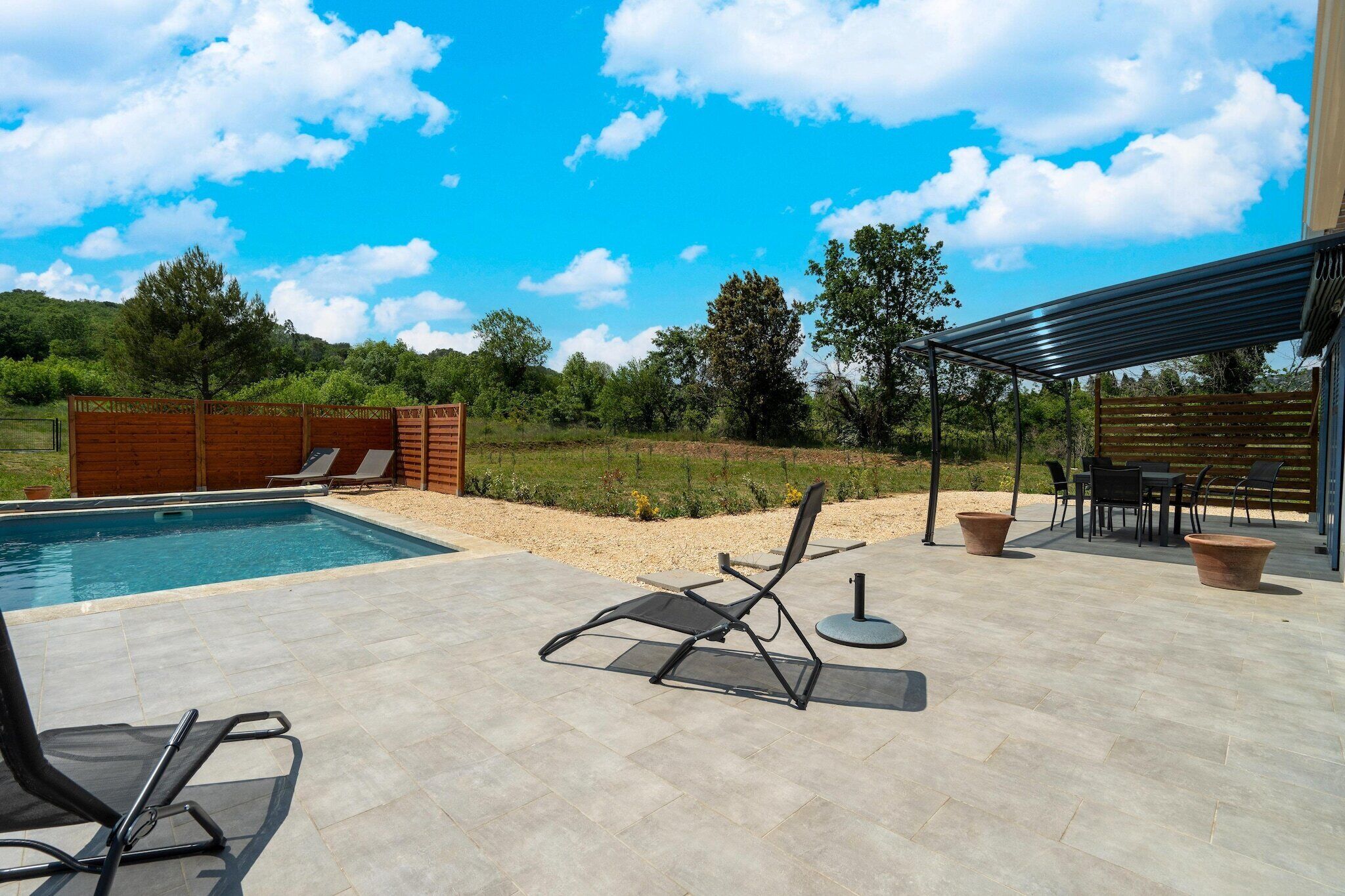 A swimming pool with lounge chairs, a covered patio area, and a view of the surrounding landscape.