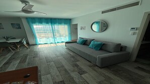 Un soggiorno moderno con un divano grigio, una ventola a soffitto, uno specchio rotondo e un'area da pranzo con sedie e tavolo.