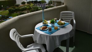 A balcony with a table set for breakfast, including croissants, fruit, and a beverage, overlooking a coastal area with buildings and greenery. - Apartment with beach view (Benalmádena)