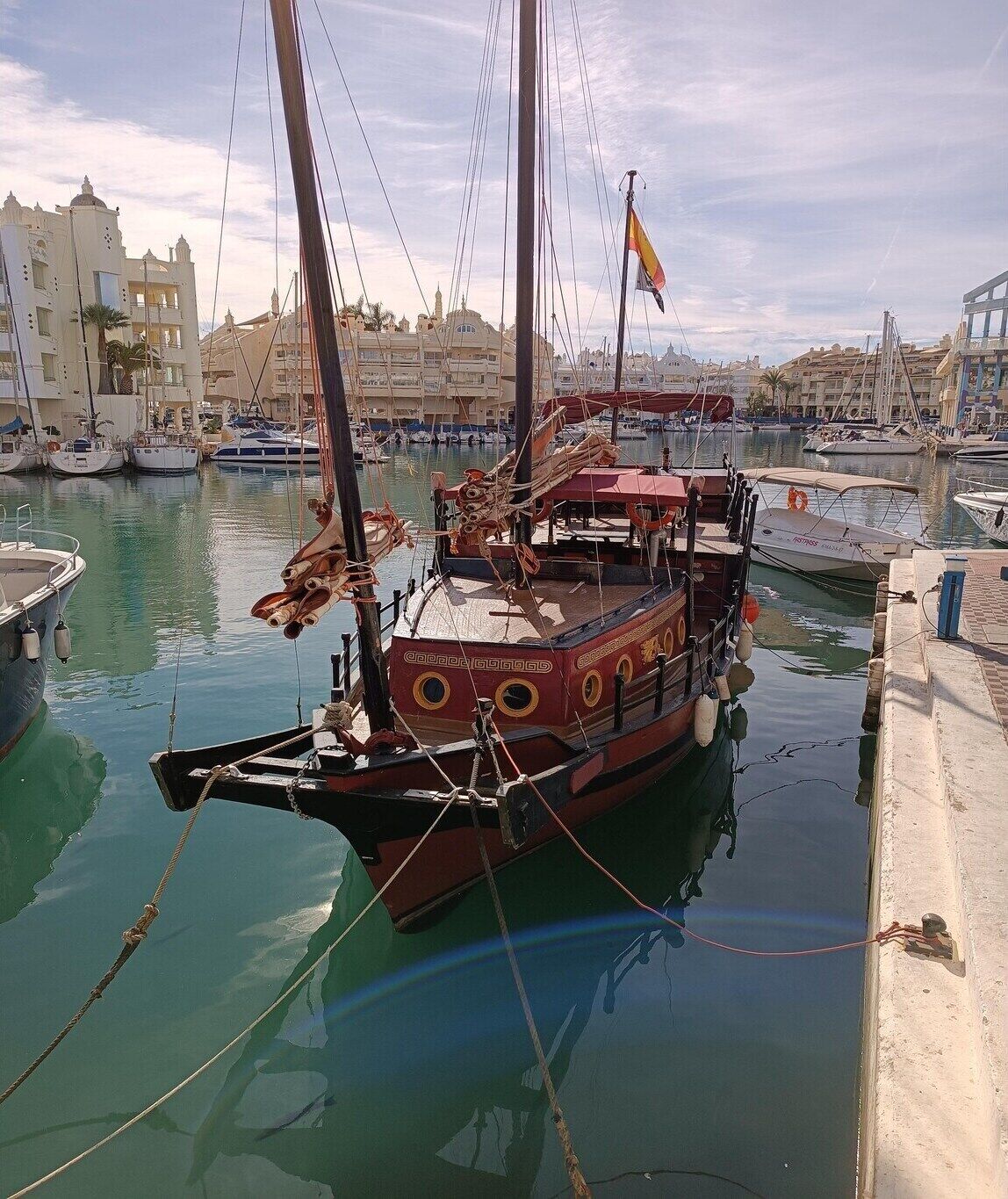 A marina with several boats docked, including a large red ship with a flag.