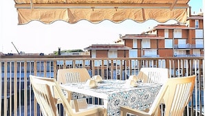 A balcony with a table and chairs, a canopy, and a view of buildings in the background.