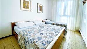 A bedroom with two beds, a large window with sheer curtains, and two framed pictures on the wall.