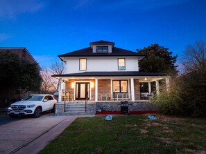 A two-story house with a porch, a car parked in front, and a clear night sky. - Colorful Large City Gatherings (Arlington)