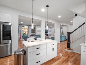 A modern kitchen with white cabinetry, a stainless steel refrigerator, and a central island with a sink. - Colorful Large City Gatherings (Arlington)