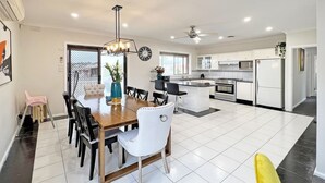 Una cocina moderna con armarios blancos, una isla central y un comedor con mesa y sillas de madera.