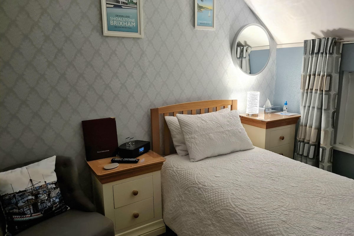 Ein ordentlich eingerichtetes Schlafzimmer mit Bett, Nachttischen, einem Spiegel und einer Wand mit strukturiertem Wandpapier.