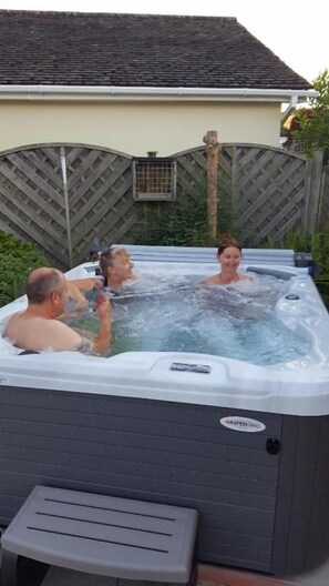 A hot tub with four people, a wooden fence, and a house in the background.