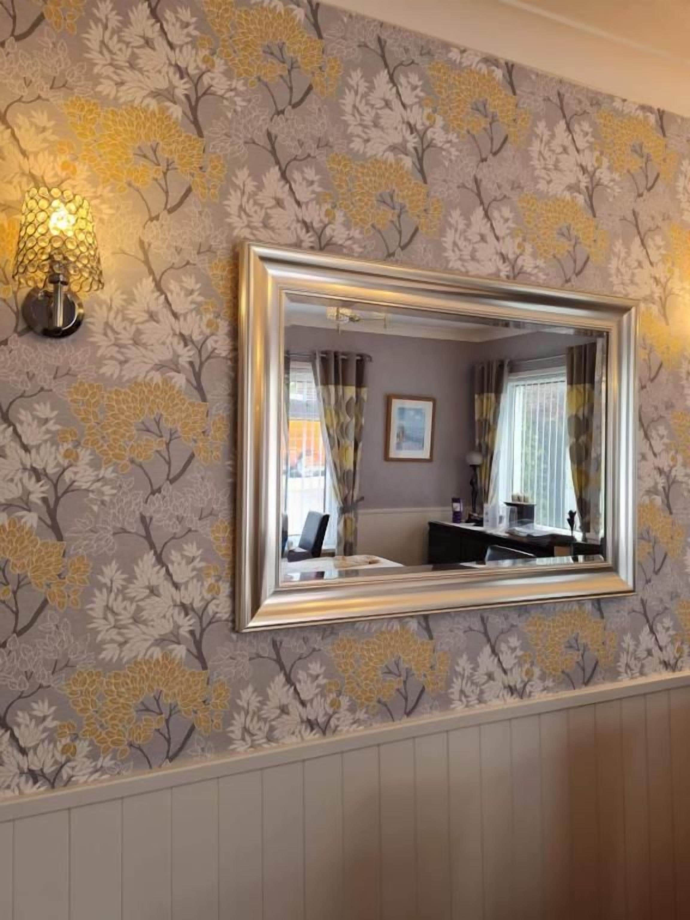 Une pièce avec un miroir fixé au mur, un papier peint à motifs et un luminaire.