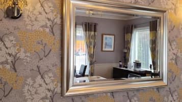 Une pièce avec un miroir fixé au mur, un papier peint à motifs et un luminaire.