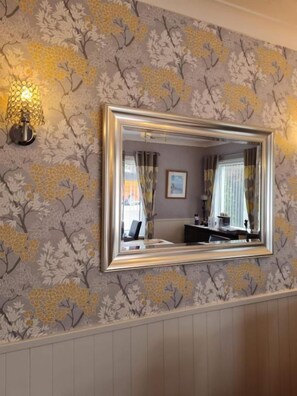 A room with a wall-mounted mirror, a patterned wallpaper, and a light fixture. - Brookside (Brixham)