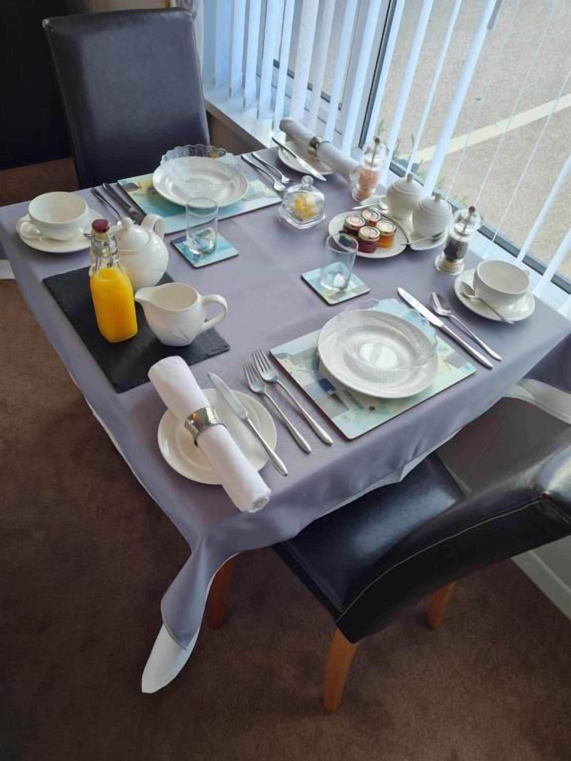 A dining table set for breakfast with plates, cups, cutlery, and a bottle of orange juice.