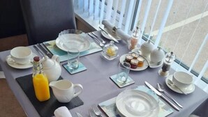 A dining table set for breakfast with plates, cups, cutlery, and a bottle of orange juice.