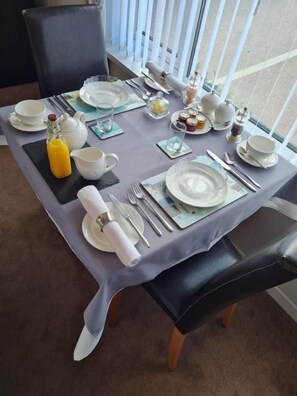 A dining table set for breakfast with plates, cups, cutlery, and a bottle of orange juice.