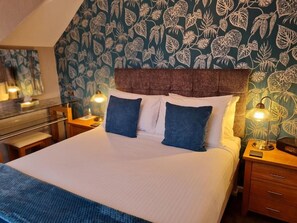 A neatly made bed with a headboard, two bedside tables with lamps, and a wall with a leafy pattern. - Brookside (Brixham)