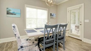 A dining area with a table and chairs, a chandelier, and two windows with blinds. - The Starfish: Near Huntington Beach State Park (Pawleys Island)
