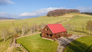 A rural house with a red roof, surrounded by green fields and trees. - The New Farmhouse (Biggar)