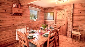A wooden cabin interior with a dining table set for four, surrounded by wooden chairs. A fire extinguisher is mounted on the wall above the table. - The New Farmhouse (Biggar)