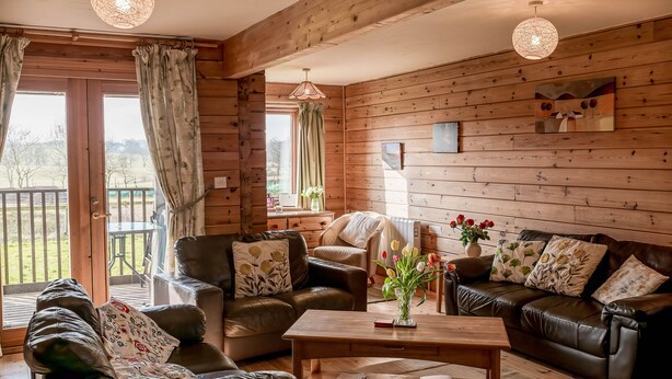 A cozy living room with leather sofas, a wooden coffee table, and a large window with curtains. - The New Farmhouse (Biggar)