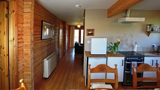 A wooden cabin interior with a kitchen area, a dining table, and chairs. - The New Farmhouse (Biggar)