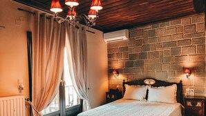 A bedroom with a wooden ceiling, a brick-patterned wall, a bed with a white quilt, and a chandelier. - Guesthouse Elena (Kalabaka)