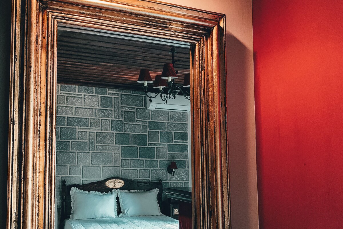 A framed mirror with a bed and brick wall behind it.