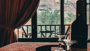 A room with a view of rocky mountains, a bottle of wine, and a tray with glasses and cutlery. - Guesthouse Elena (Kalabaka)