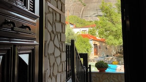 A stone archway leading to a courtyard with a pool, surrounded by greenery and a mountainous backdrop. - Guesthouse Elena (Kalabaka)