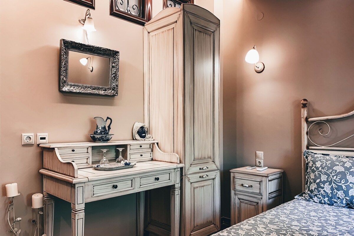 A bedroom with a bed, a dresser, a vanity with a mirror, and a nightstand.