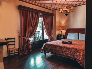 A hotel room with a bed, a chair, a nightstand with a lamp, and a window with curtains. - Guesthouse Elena (Kalabaka)