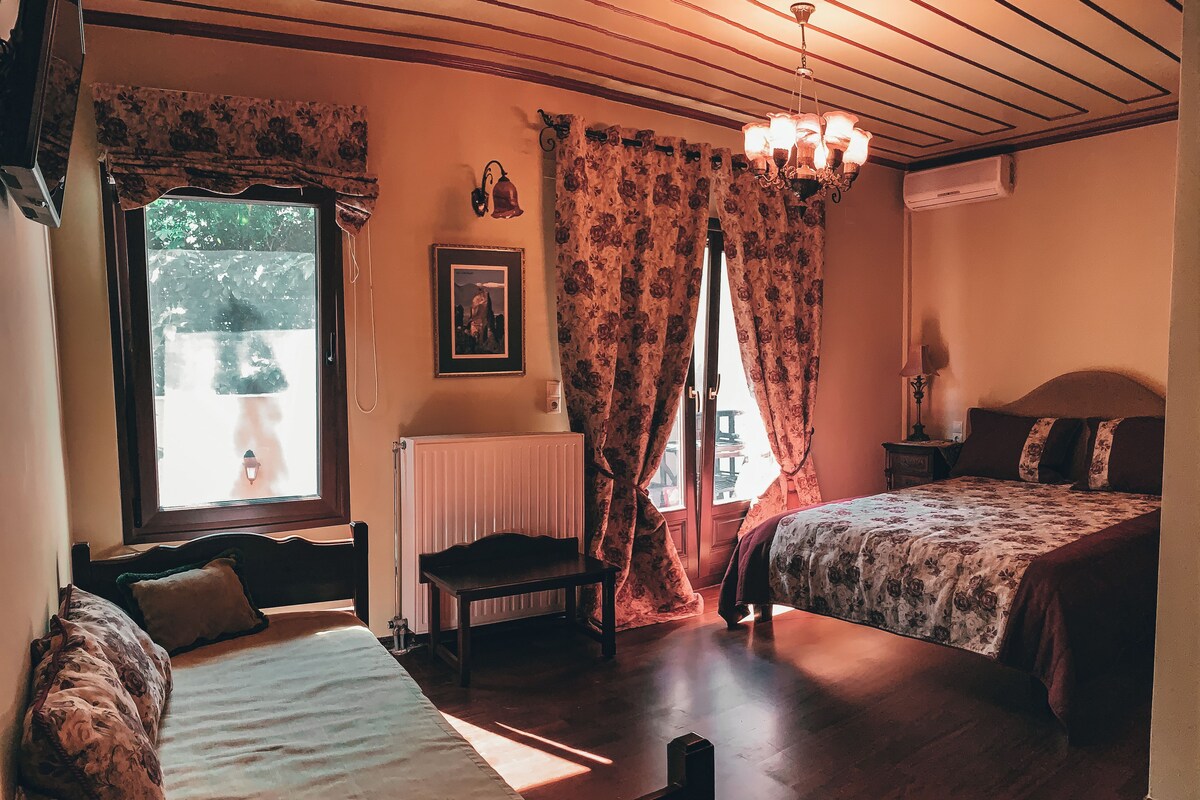 A room with two beds, a radiator, a window with curtains, a chair, a table, and a chandelier.