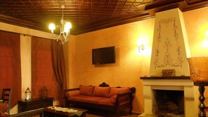 A cozy living room with a fireplace, a sofa, a coffee table, and a television mounted on the wall. - Guesthouse Elena (Kalabaka)