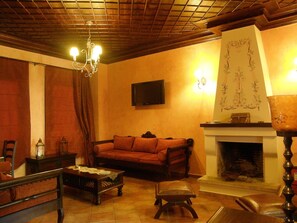 A cozy living room with a fireplace, a sofa, a coffee table, and a television mounted on the wall. - Guesthouse Elena (Kalabaka)