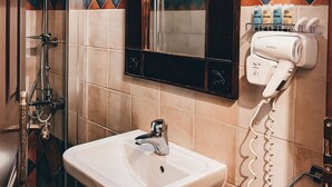 A bathroom with a sink, mirror, shower, and hairdryer. - Guesthouse Elena (Kalabaka)