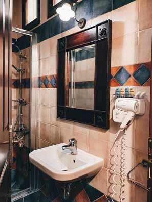 A bathroom with a sink, mirror, shower, and hairdryer.