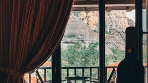 A room with a large window overlooking a mountainous landscape, a bottle of wine, and a tray with glasses and cutlery. - Guesthouse Elena (Kalabaka)