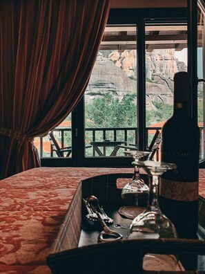 A room with a large window overlooking a mountainous landscape, a bottle of wine, and a tray with glasses and cutlery.