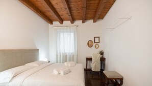 A bedroom with a large bed, a wooden headboard, a desk with a chair, and a bench. - Residenza Cappello (Verona)