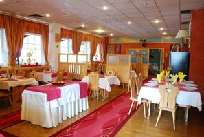Un espace repas avec des tables dressées pour le service, des chaises en bois et une moquette rouge.