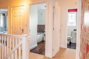 A hallway with a white door leading to a bathroom with a shower, toilet, and sink.