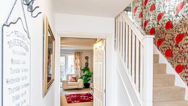 Un escalier orné d’un papier peint à motifs floraux, une porte blanche et un couloir avec un tapis rouge.