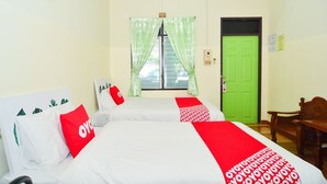 A hotel room with two beds, a green door, and a window with green curtains.
